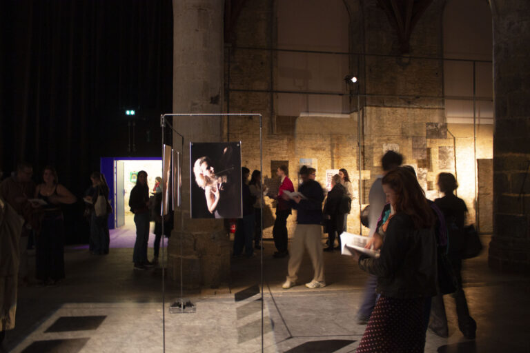 Des personnes dans un lieu sombre regardent des oeuvres éclairées
